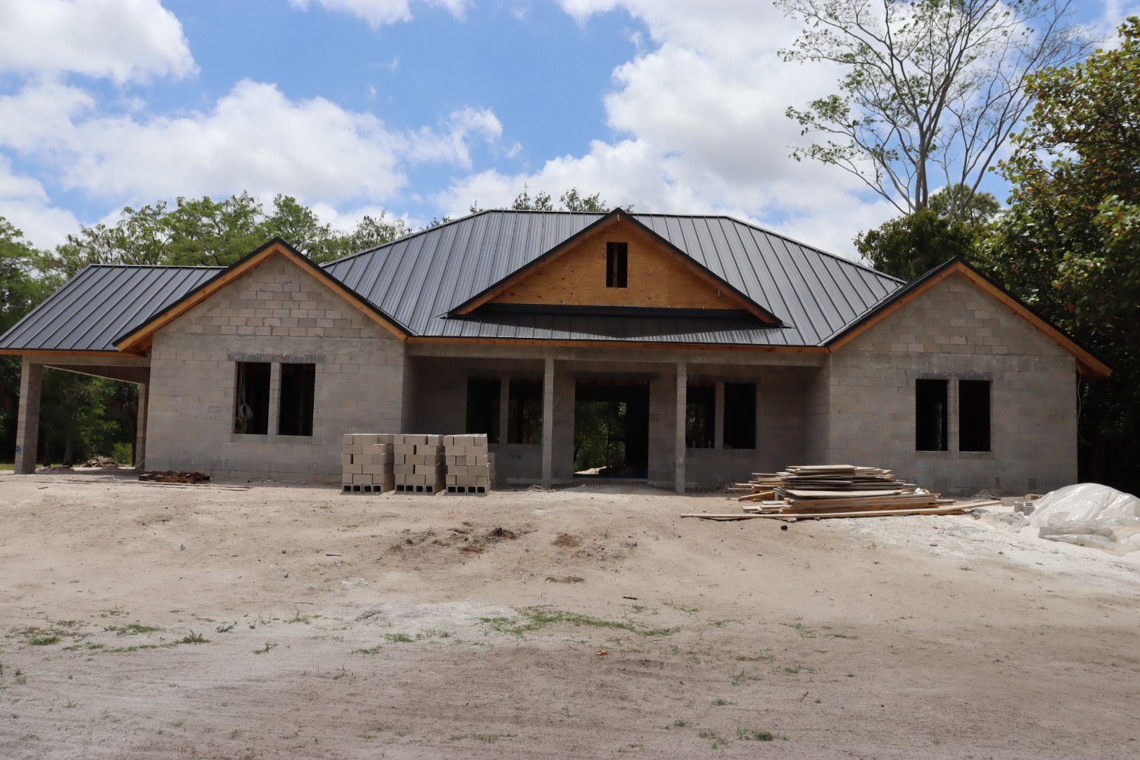 House under construction with gray walls, black roof, and wooden accents. Sunny day.