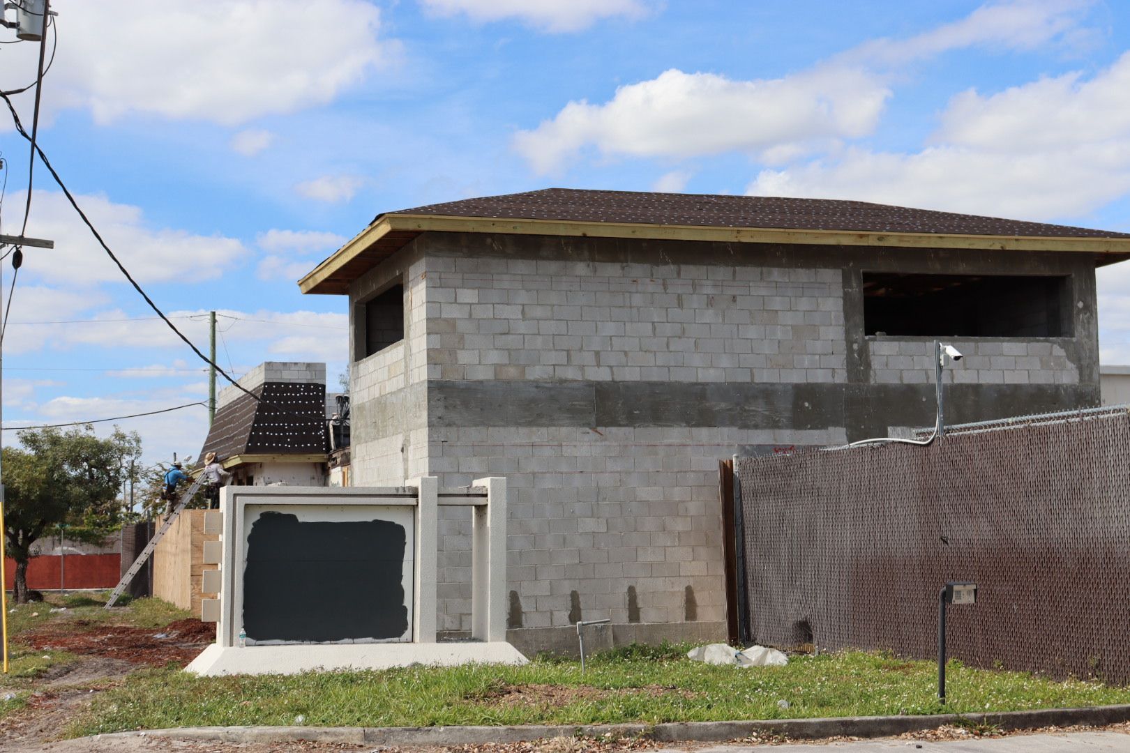 Two-story unfinished concrete building with window openings, next to a sidewalk and a utility box.