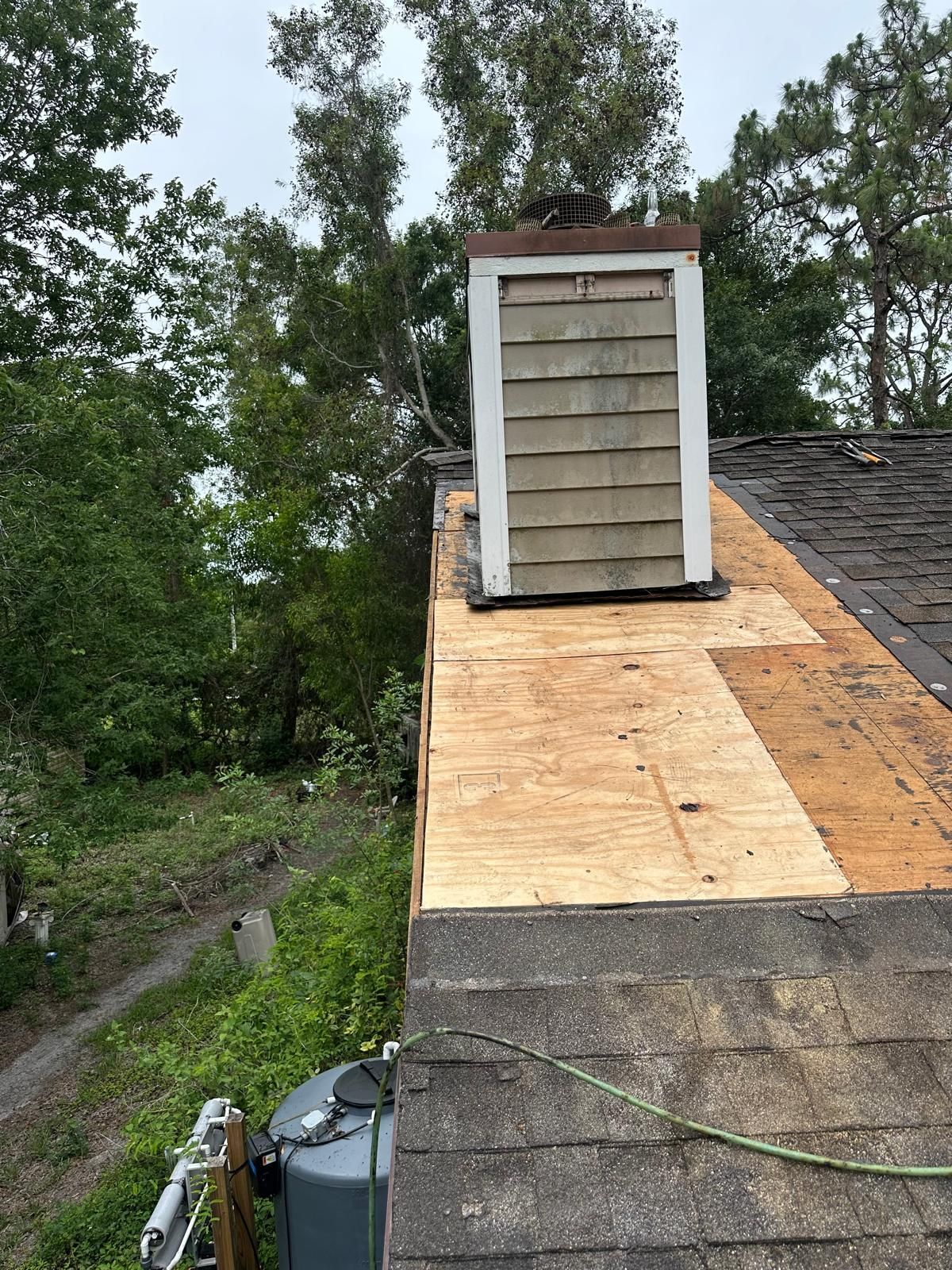 Chimney on a partially re-roofed house with new plywood, surrounded by trees and greenery.