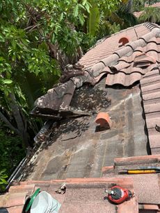 Damaged tile roof section with missing tiles, likely from storm.