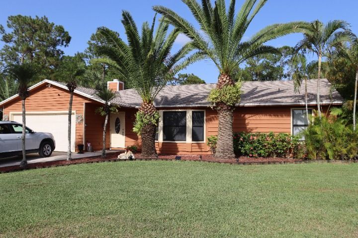 Brown house with palm trees in front; a car sits in the driveway.
