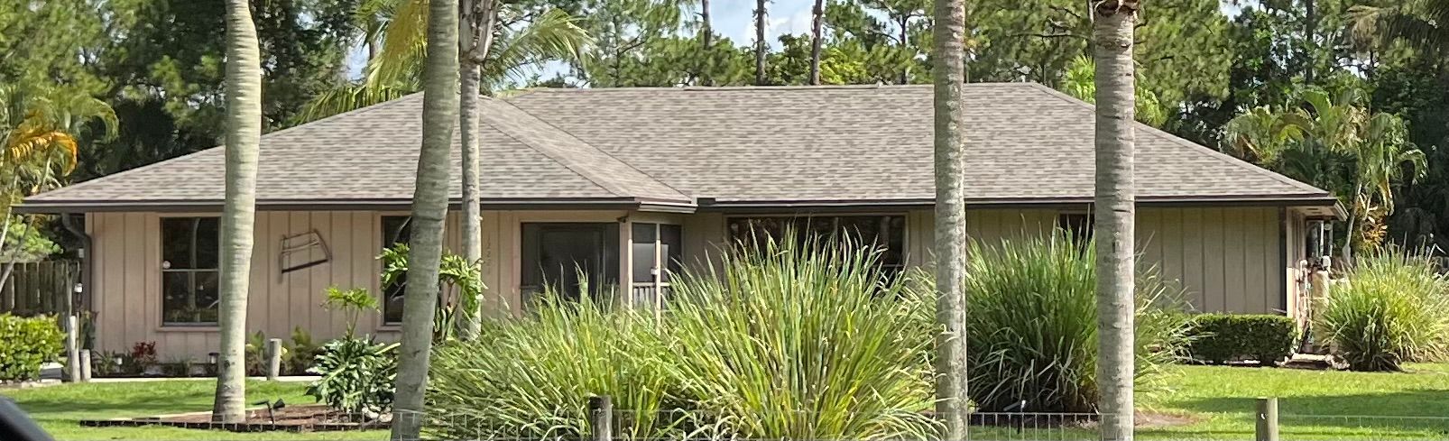 Tan house with a gray roof and surrounded by trees and green grass.