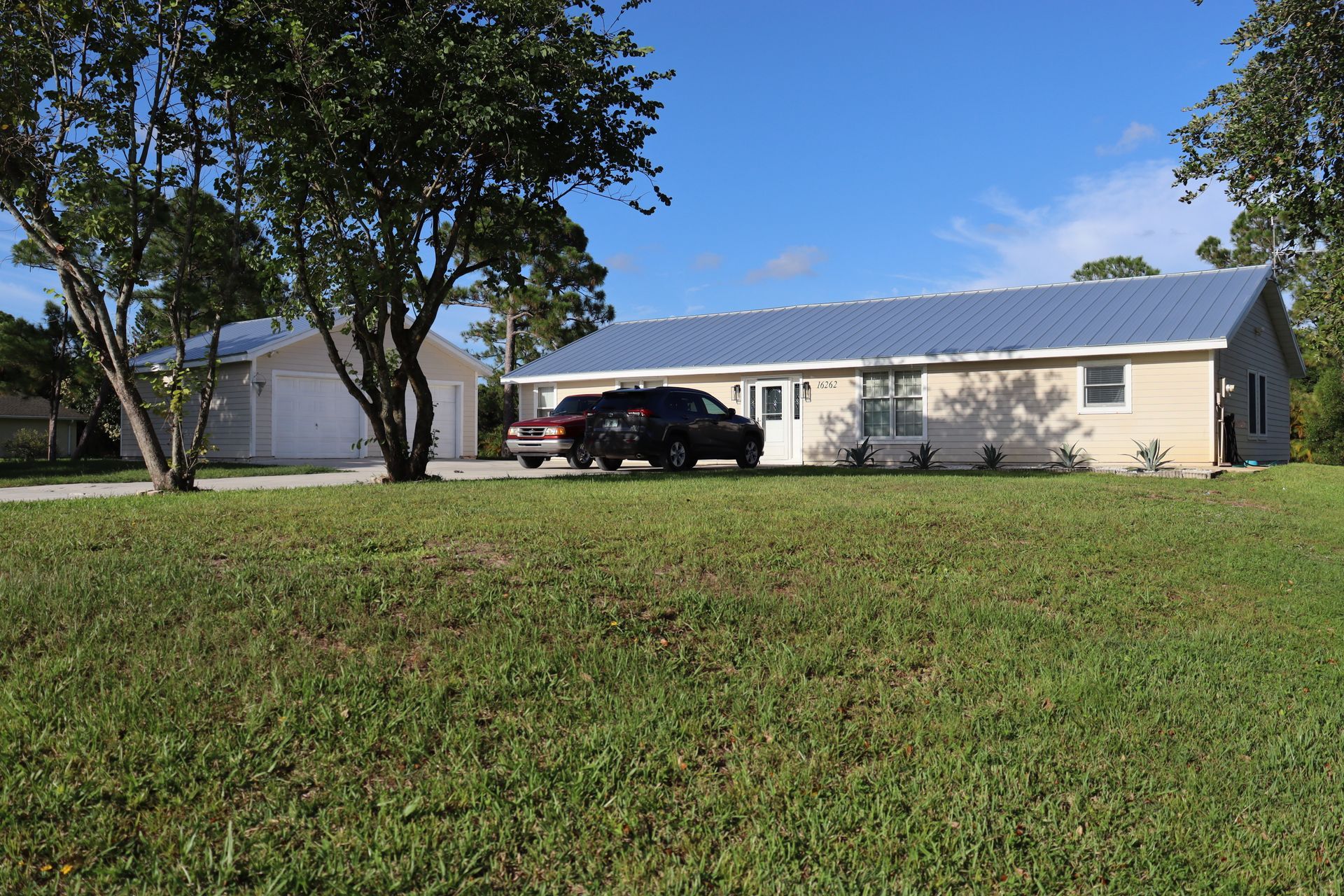 House with blue roof and two cars parked in front, on a grassy lawn.