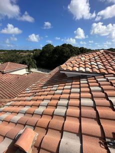 Red tile roof against a blue sky with white clouds. Trees and a road are in the background.