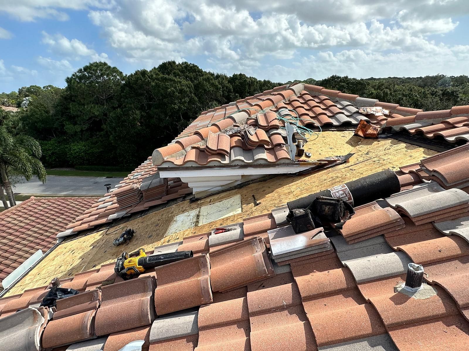 Rooftop with missing tiles undergoing repair, showing exposed underlayment and tools on a sunny day.