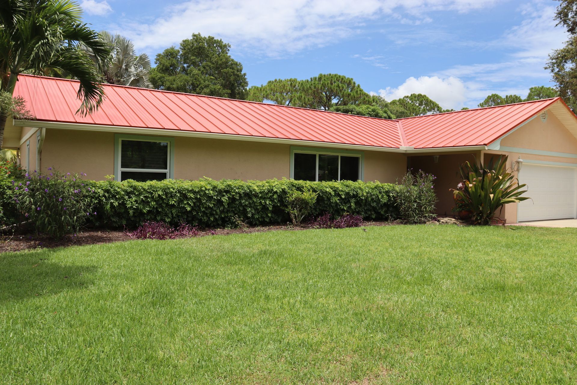 Tan house with red tile roof, green lawn, and shrubs.