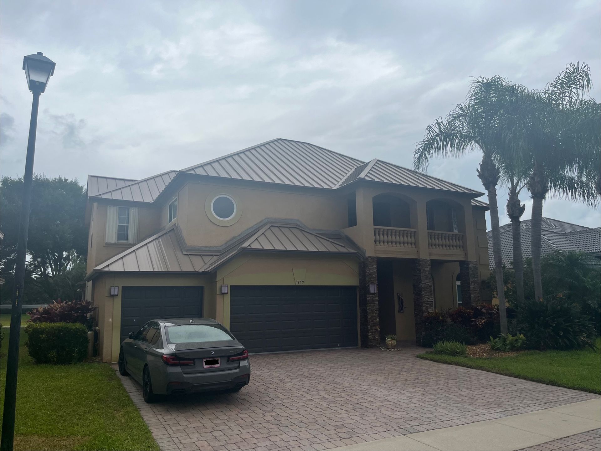 Two-story tan house with a car parked in the driveway, on a cloudy day.