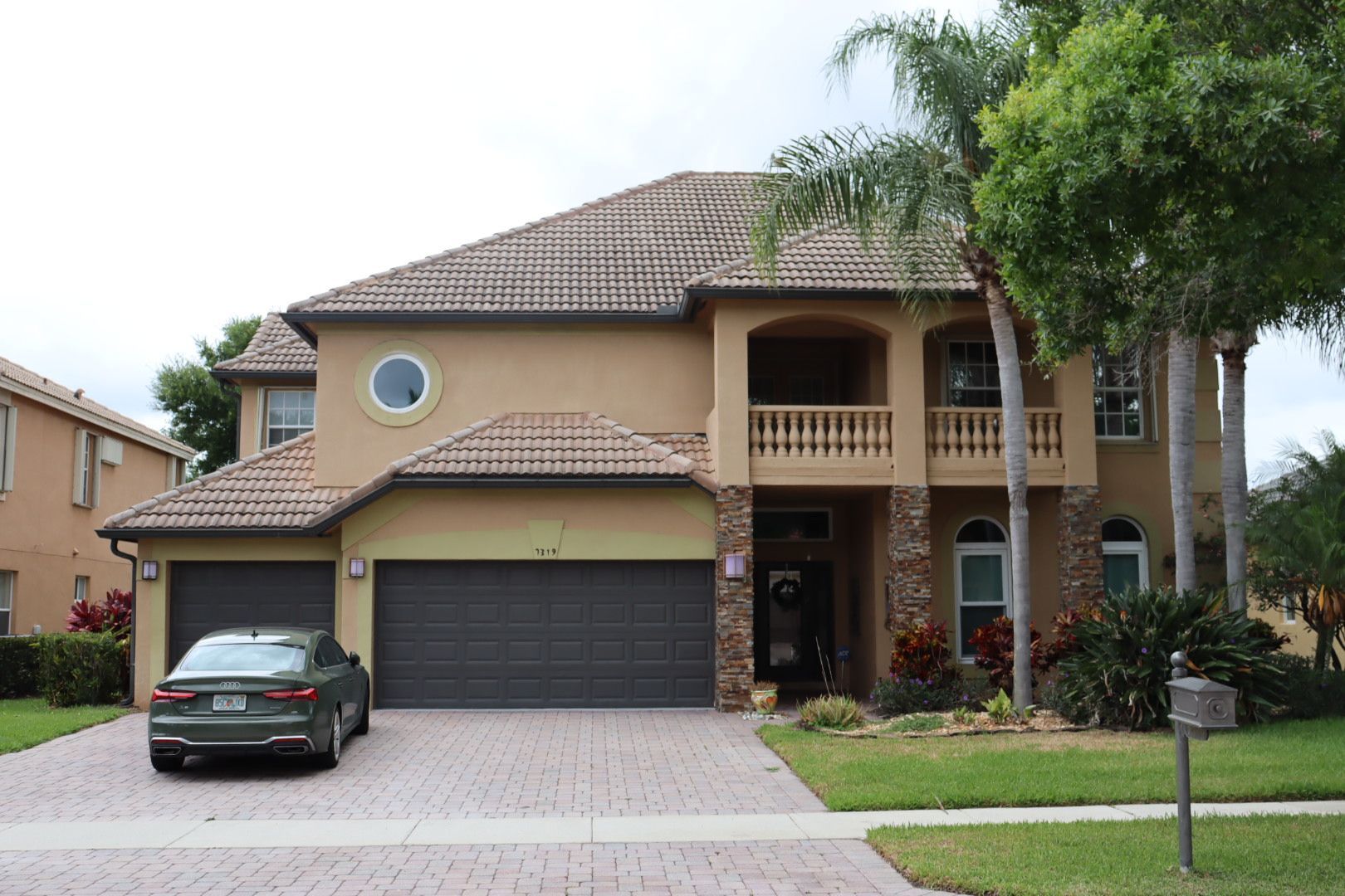 Two-story beige house with a gray garage door, a car parked in front, and a landscaped lawn.
