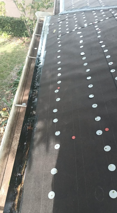 A dark, flat roof with metal fasteners in neat rows, near a gutter.