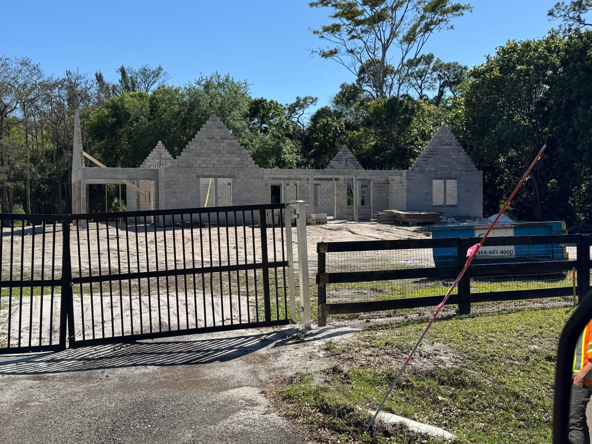 Construction of a single-story house with a brick facade behind a black gate on a sunny day.