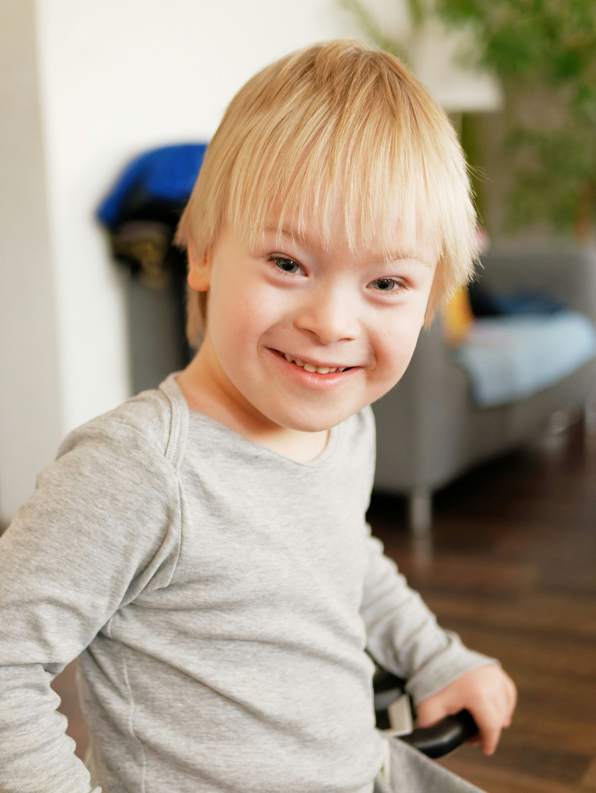 Smiling child in a gray shirt indoors, with a blurred chair and couch in the background