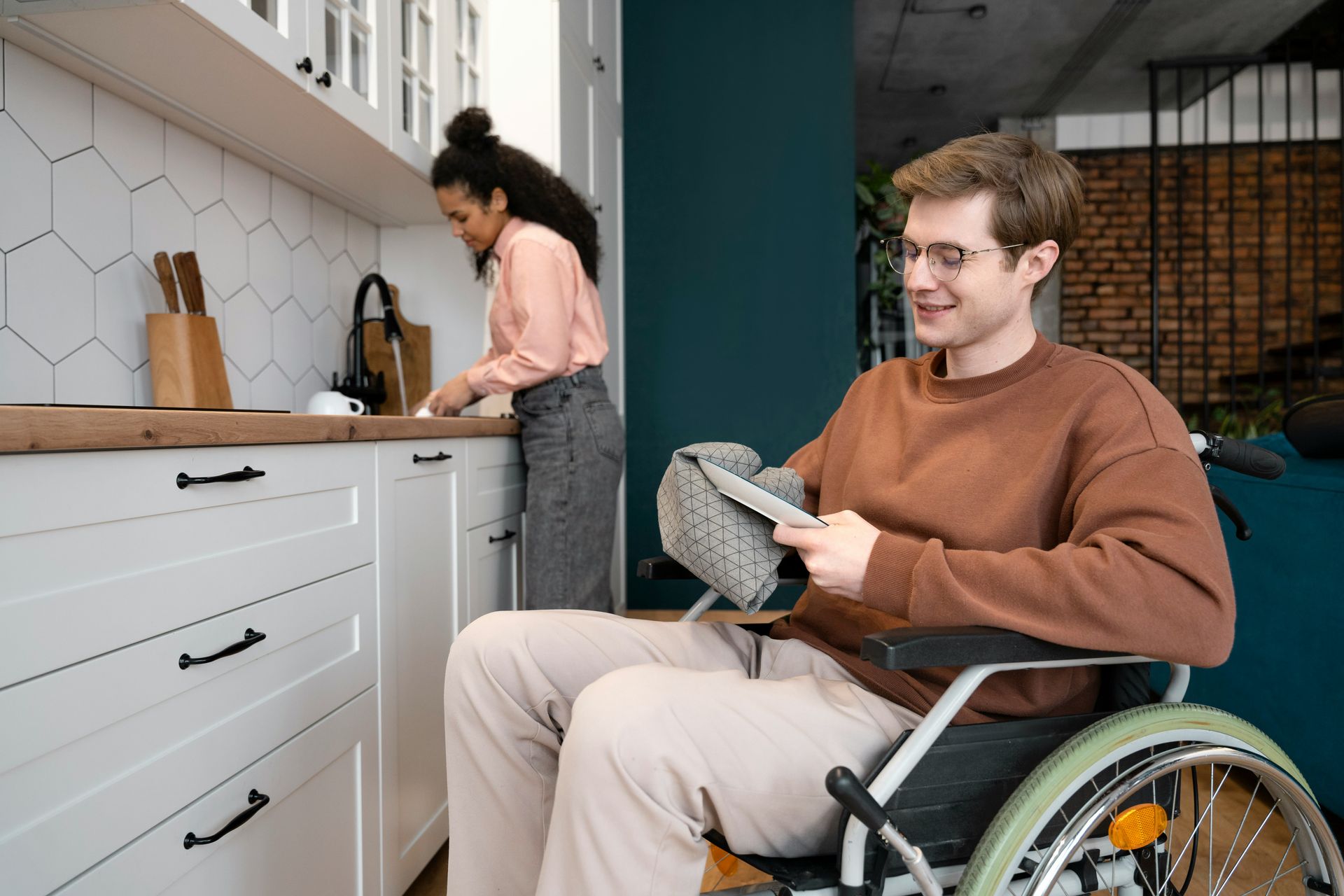 Man in wheelchair holding a bowl in a modern kitchen while a woman prepares food at the counter
