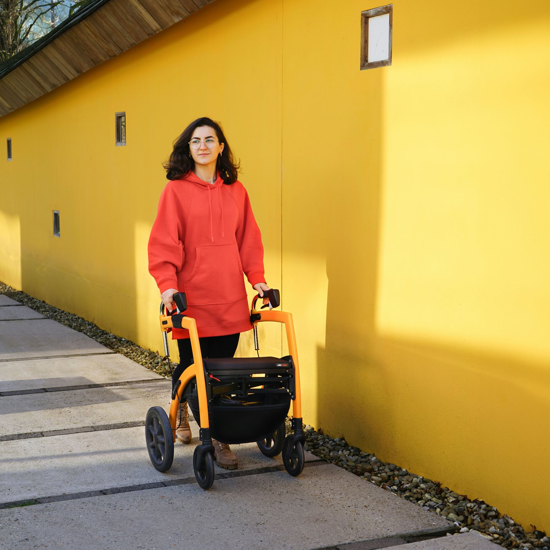 Person walking outdoors with a walker beside a bright yellow wall.