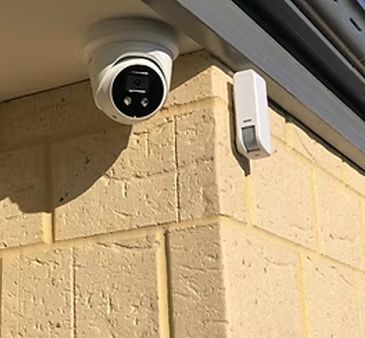 Security camera and motion sensor mounted on a light brick wall.