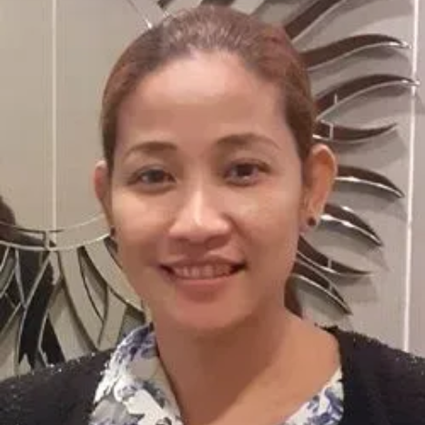Woman smiling, wearing floral top and black jacket, near a decorative wall.