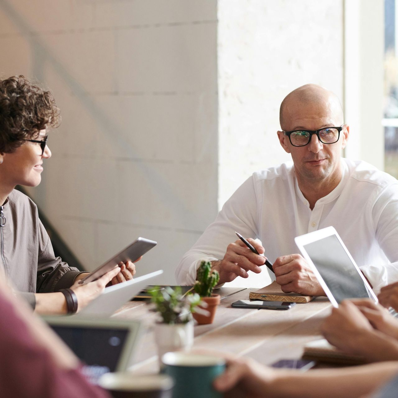 People in a meeting at a table, using tablets and a pen. A window is in the background.