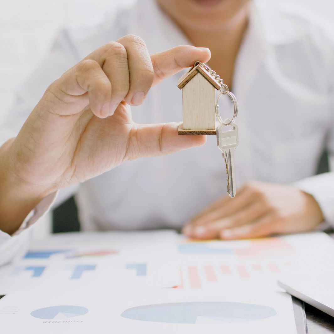 Person holding a house-shaped key chain over documents with charts and graphs.