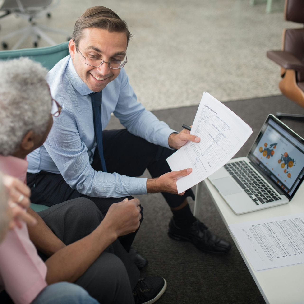 Man in suit showing documents to another person with laptop and graph.