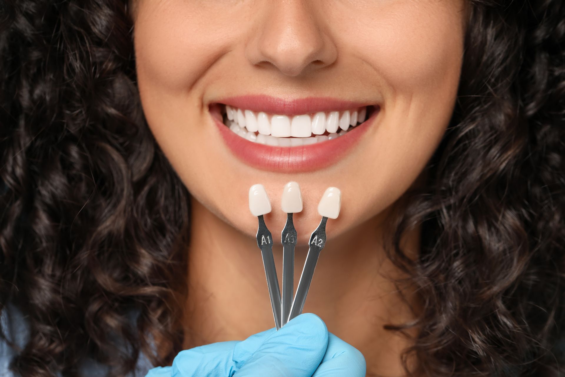 Dentist matching veneer shade guide to woman's smile.