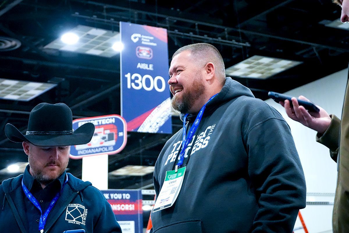 Two men in cowboy hats talking at an indoor event booth with a large “1300” sign.
