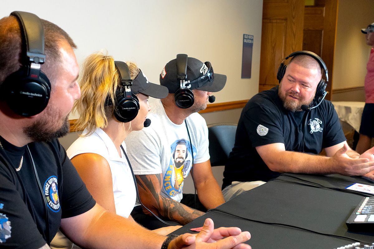 Four people wearing headsets sit around a table in a conference room, talking and smiling.