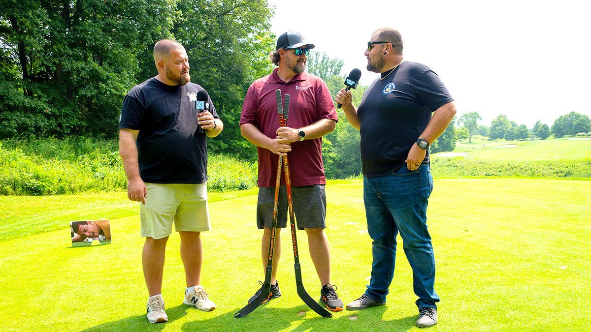 Three people standing on a golf course, talking with clubs in hand, one holding a drink.