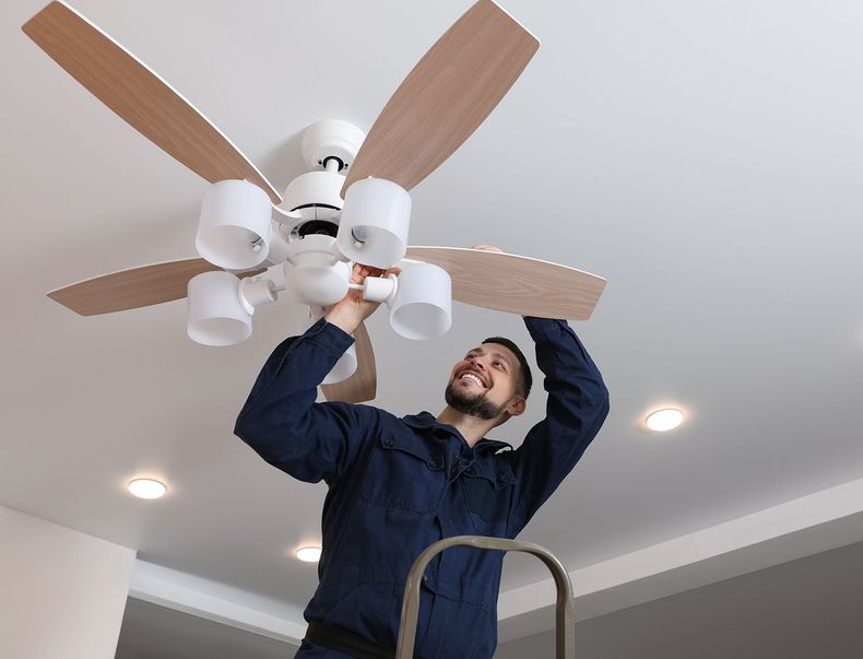 Electrician installing a ceiling fan with wooden blades Electrician installing a ceiling fan with wooden blades