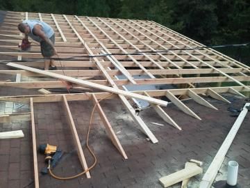 Worker framing a roof with wooden trusses and joists on a construction site.