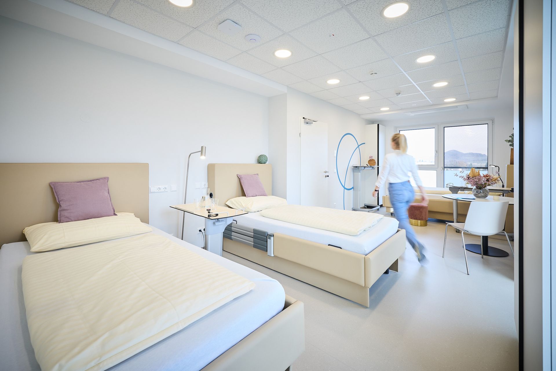 Eine Frau geht durch ein Zimmer mit zwei Betten und einem Schreibtisch.