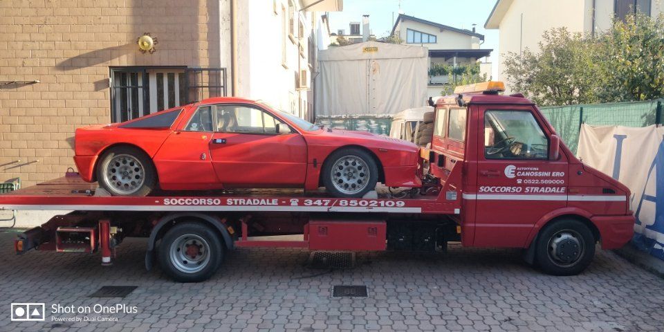 Auto sportiva rossa su un carro attrezzi con pianale in una stretta via residenziale