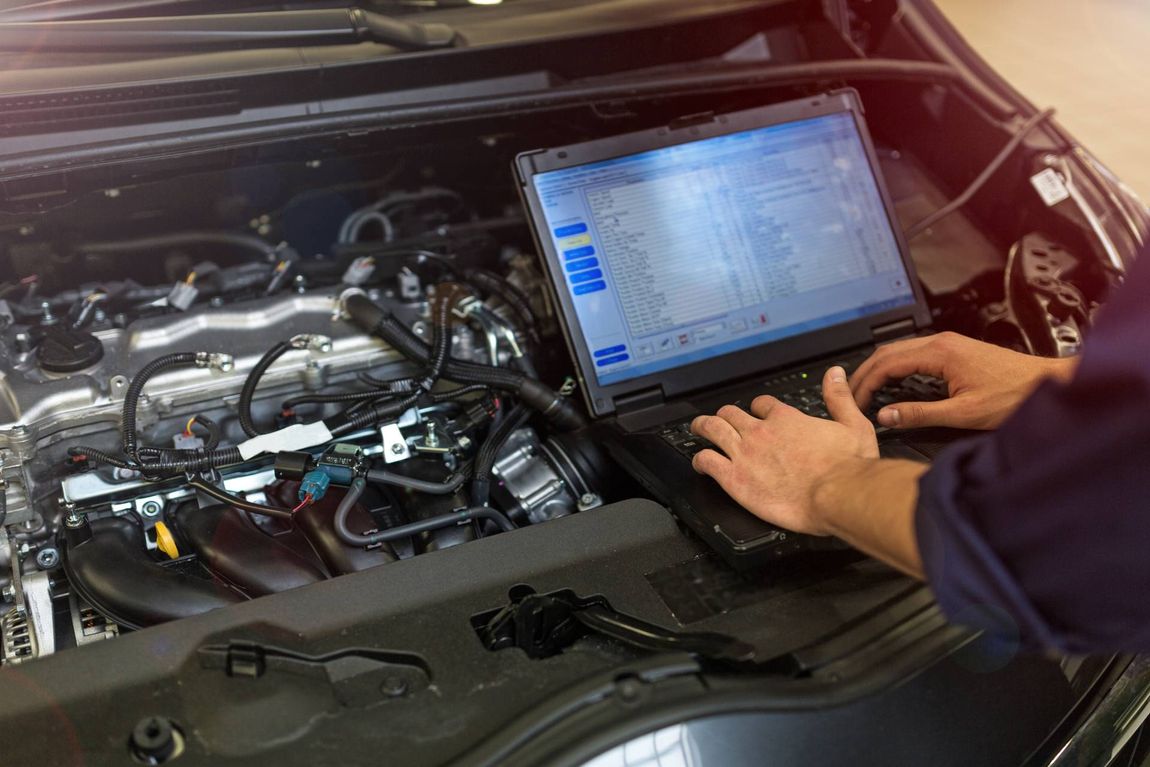 Un meccanico utilizza un computer portatile per diagnosticare un problema al motore di un'auto nel vano motore aperto.