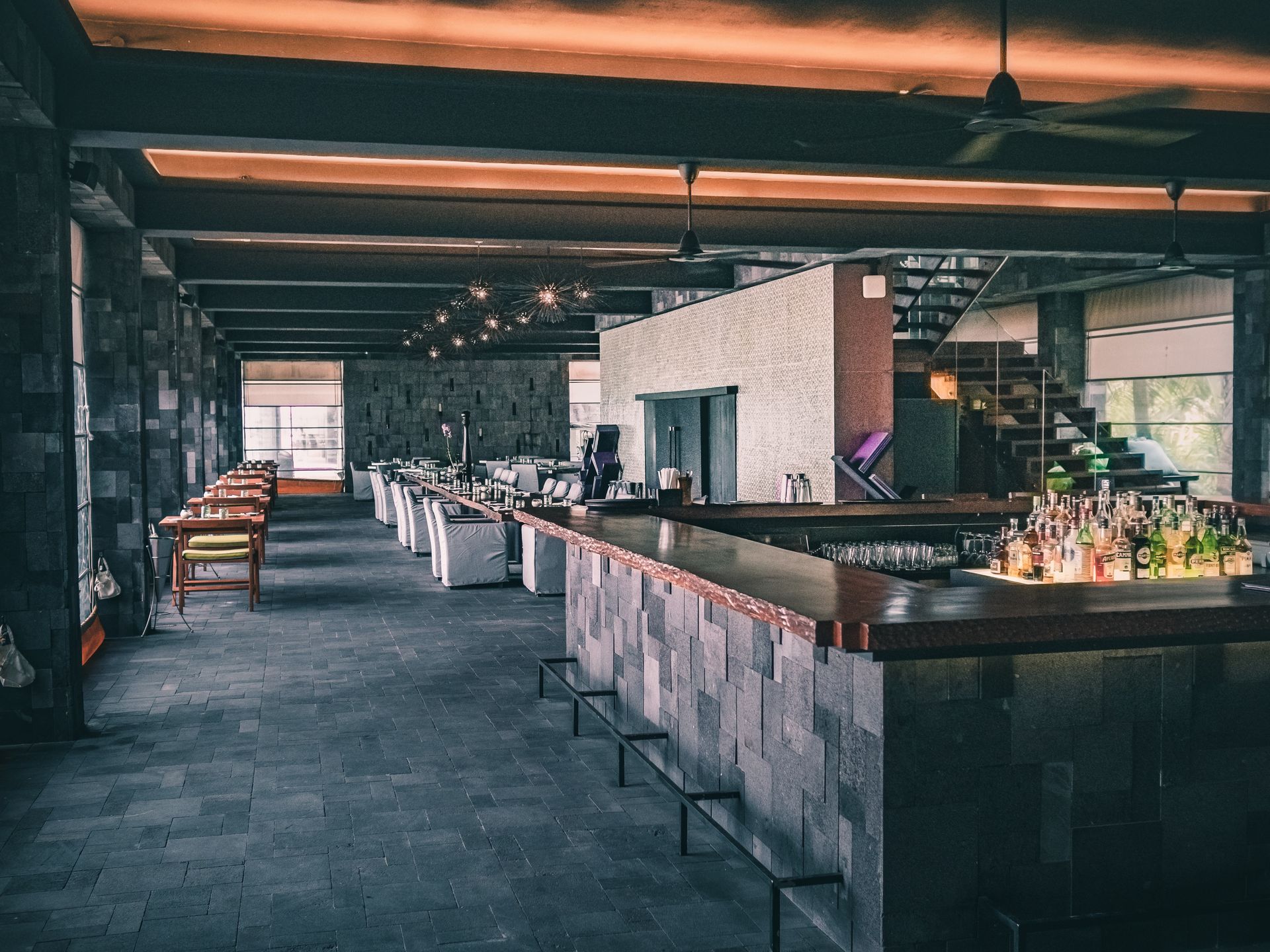Interior view of a modern restaurant with a bar, tables, and stone walls.