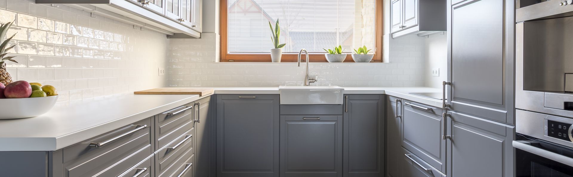 A kitchen with gray cabinets , stainless steel appliances , a sink , and a window.