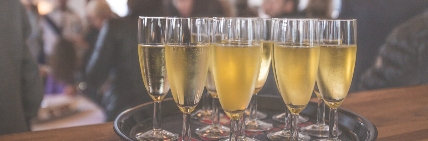 Four champagne flutes filled with sparkling wine on a table, with a blurred festive background