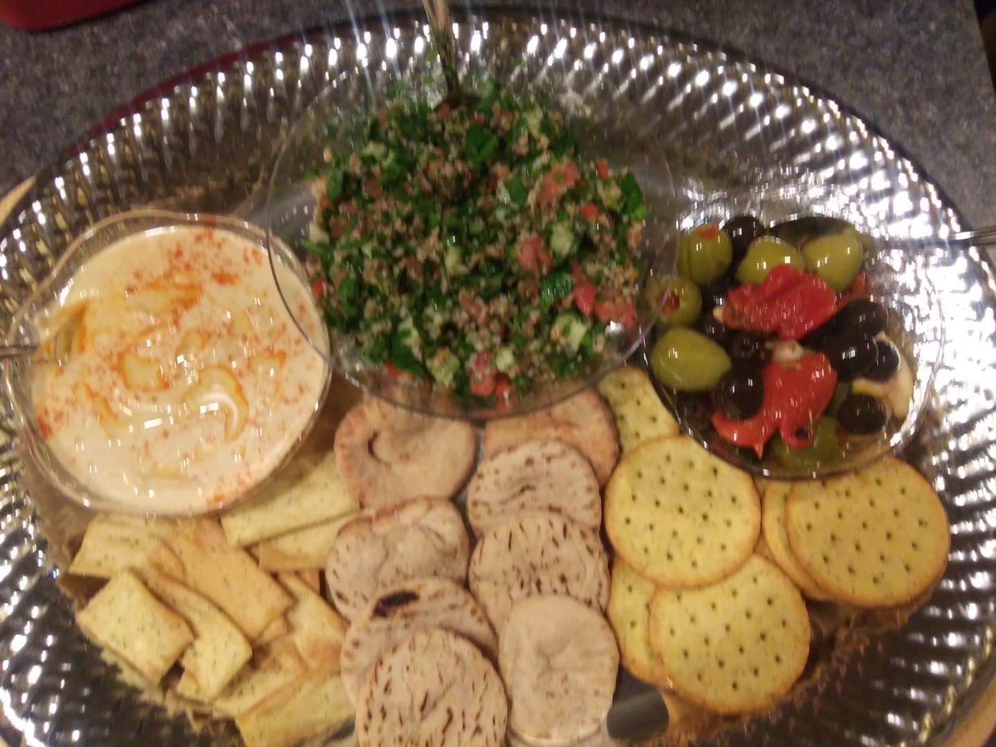 Assorted appetizers on a platter, including dip, chopped salad, olives, crackers, and toasted bread slices.