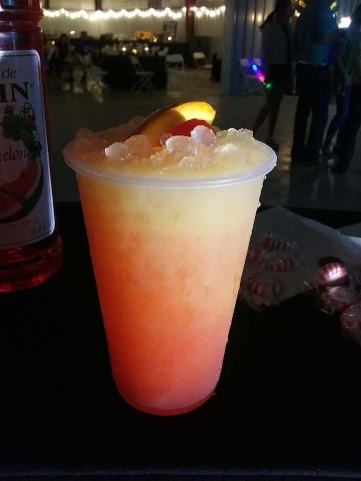 Translucent red-to-yellow drink in a clear cup with gummy candies on top at a dim event table