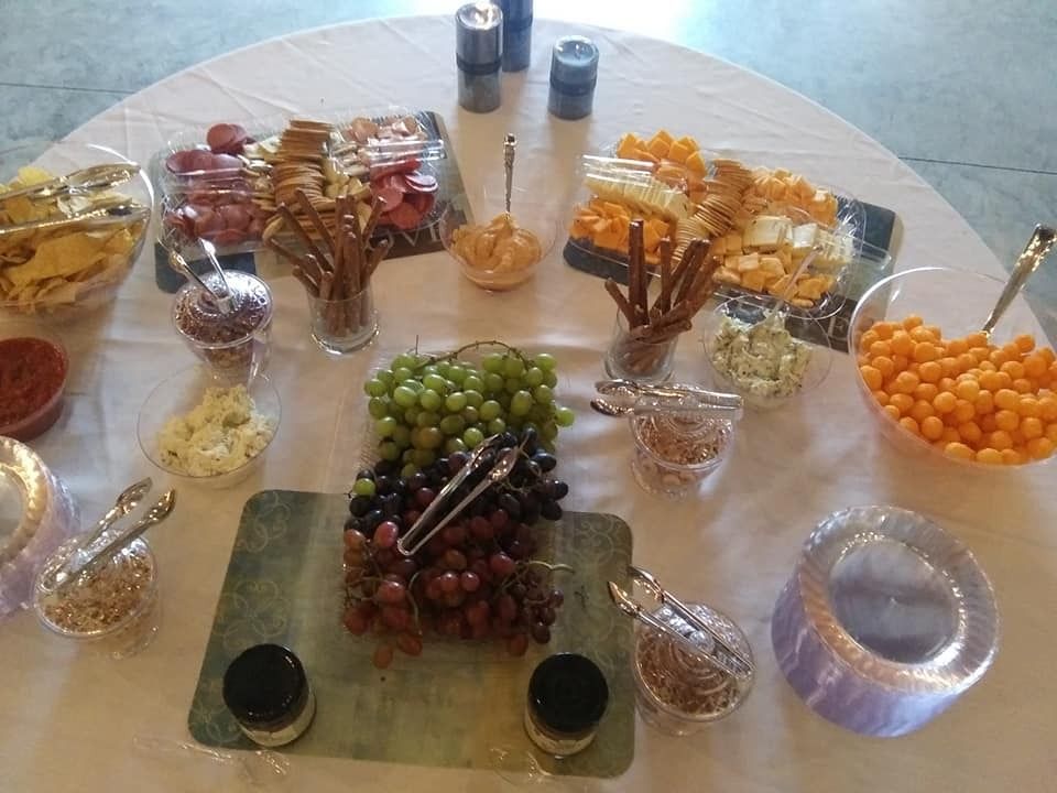 Assorted snacks and fruit arranged buffet-style on a glass table with bowls and jars of candies and grapes.