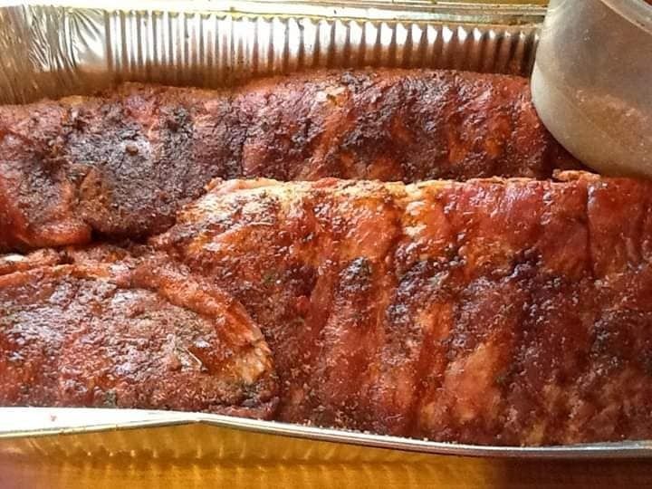 Two glazed racks of ribs in a foil tray, browned and sauced.