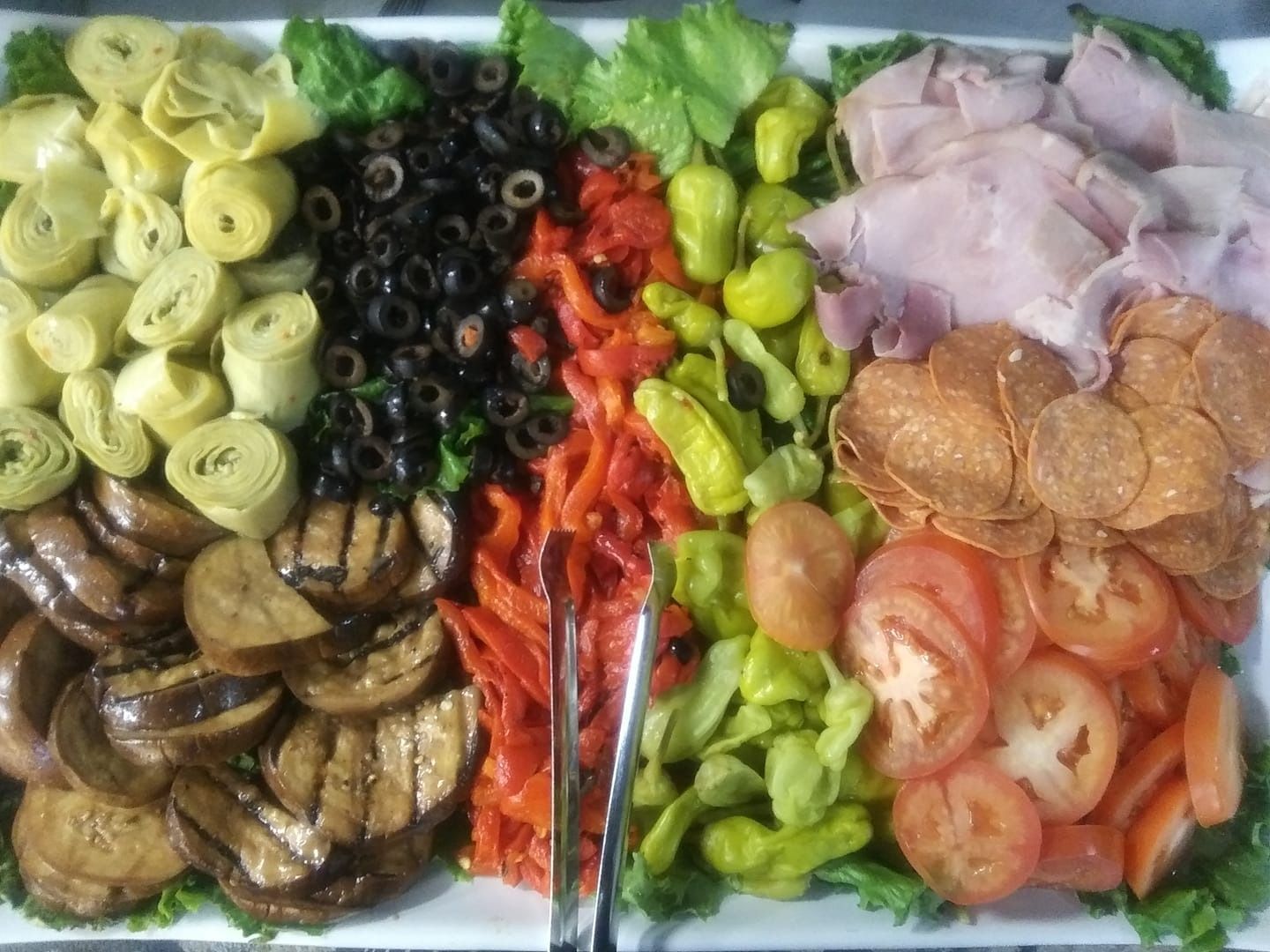 Assorted vegetables arranged in colorful rows on a platter, including olives, tomatoes, cucumbers, artichokes, and mushrooms