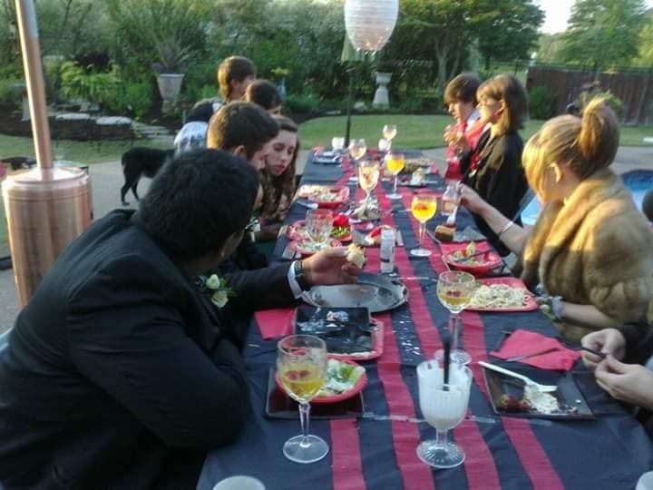 People seated around a long outdoor dining table with drinks and plates at a garden gathering