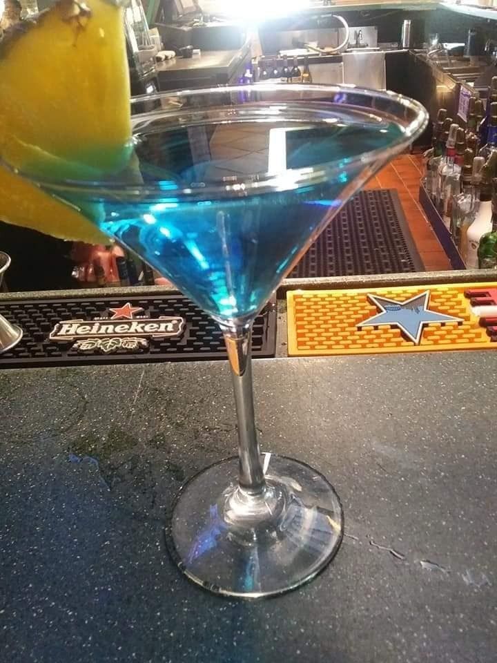 Blue martini in a stemmed glass with a lime garnish on a bar counter