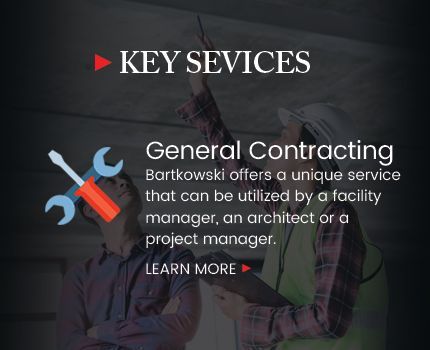 A man is holding a wrench and a screwdriver while standing next to another man.