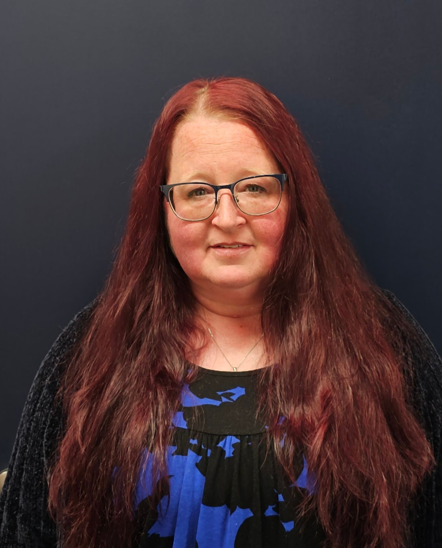 A woman with long red hair and glasses is wearing a blue and black dress.