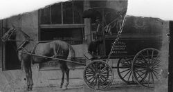 Horse-drawn wagon parked outside a building, with a covered carriage and large wheels.