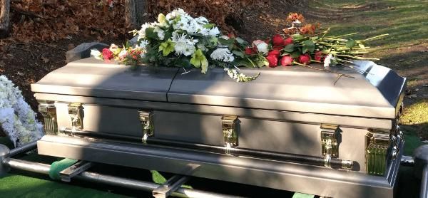 White casket with flowers on a green bier, outdoors in sunlight
