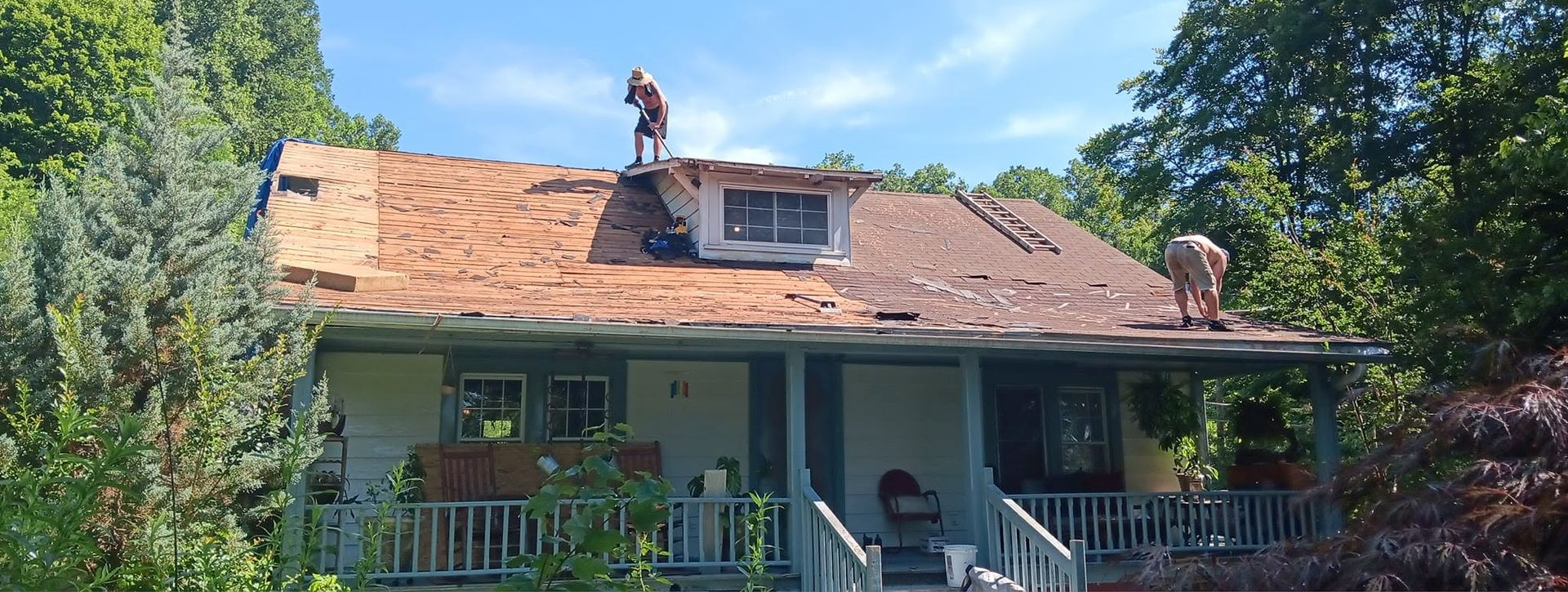 House with roof workers under repair, surrounded by trees and a porch