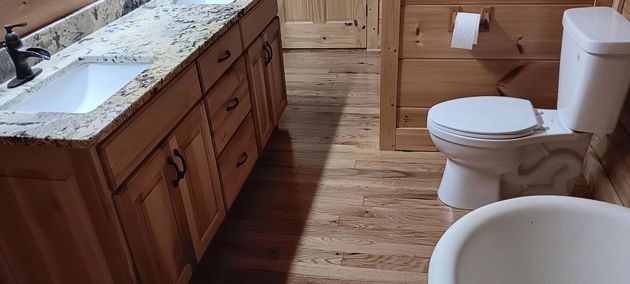 Bathroom with wood vanity, white toilet, and tub on a wood floor.