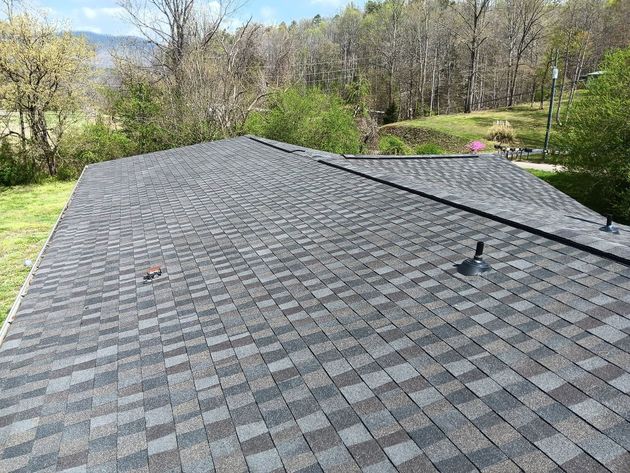 Shingled roof with vents, viewed from above, with trees and a grassy yard in the background