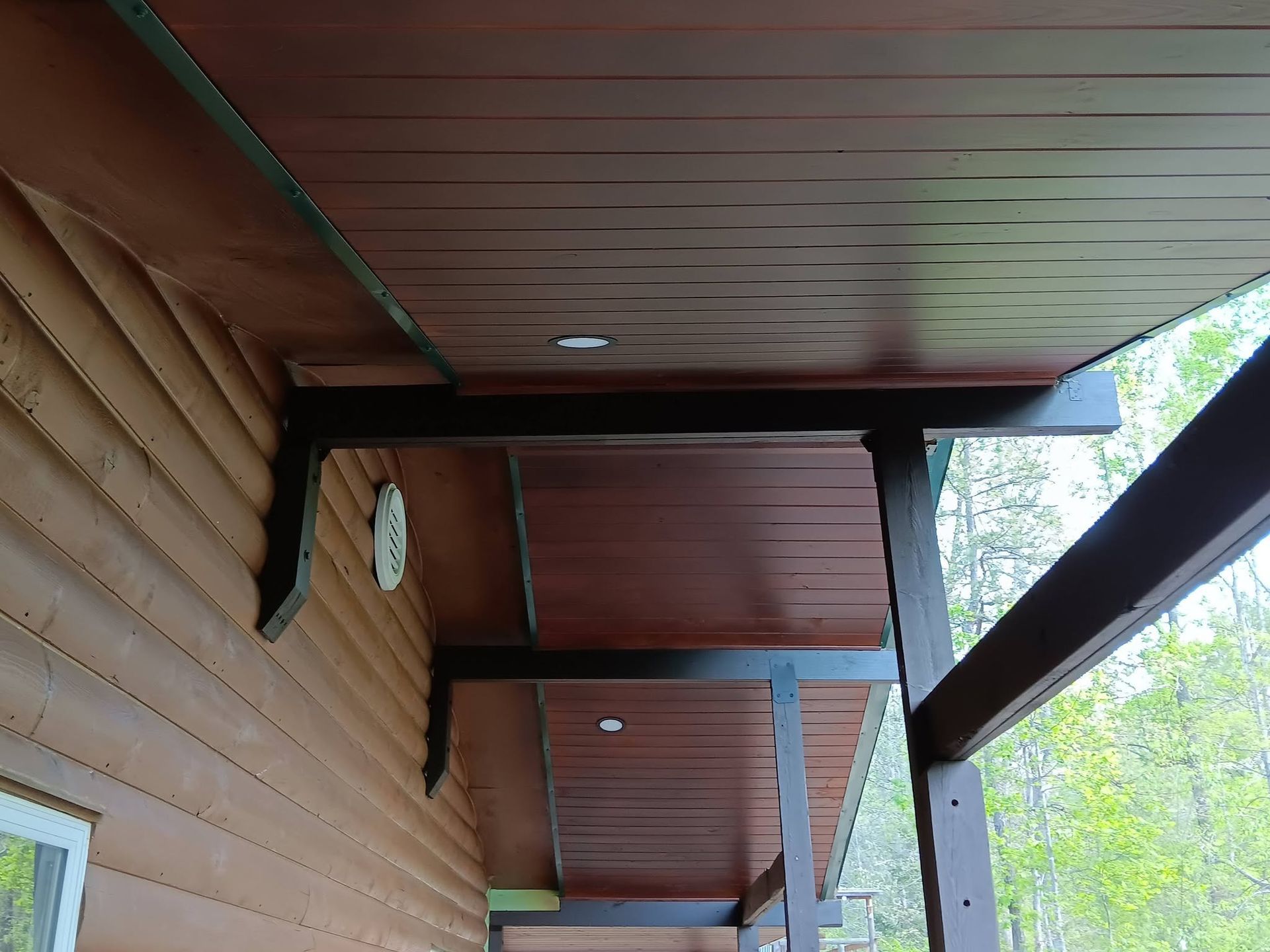 Wooden porch ceiling with exposed beams and a slanted support post beside trees outside
