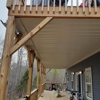 Covered back deck under construction with wooden support beams and house siding alongside bicycles.